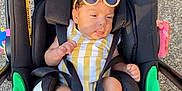 Maeva participe au concours pour gagner de l'argent avec cette photo : baby, child, stroller, sunglasses, outdoor, sunlight, yellow_striped_clothing, black_stroller, infant, feet, legs, head, hair, seatbelt, wheels, pavement, relaxing, cute, summer, fashion