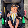 baby, child, stroller, sunglasses, outdoor, sunlight, yellow_striped_clothing, black_stroller, infant, feet, legs, head, hair, seatbelt, wheels, pavement, relaxing, cute, summer, fashion