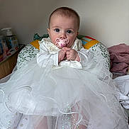 Lilyana a rejoint le concours — aidez-le/la à gagner de superbes lots ! baby, child, pacifier, white_dress, tutu, sitting, cushion, indoor, infant, hands, feet, clothing, cute, wide_eyes, portrait, soft_lighting, baby_supplies, comfort, person, nursery