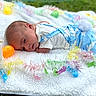 baby, infant, blue_clothing, bunny_theme, plush_toy, llama, white_blanket, colorful_garland, easter_eggs, outdoor, grass, lying_down, cute, soft_texture, festive, holiday, child, portrait, summer, playful