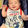 baby, infant, smiling, sleeveless_shirt, captain_mickey, car_seat, patterned_fabric, blue, red_trim, happy, cute, child, person, sitting, face, skin, hand, clothing, indoor, portrait