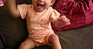 Ariana joined the competition — help win amazing prizes! baby, child, infant, smiling, laughing, sitting, couch, sofa, cushion, indoor, portrait, peach_outfit, bow, socks, toy, living_room, happy, playful, arms_raised, cozy