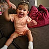 baby, child, infant, smiling, laughing, sitting, couch, sofa, cushion, indoor, portrait, peach_outfit, bow, socks, toy, living_room, happy, playful, arms_raised, cozy