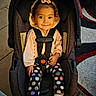 child, baby, toddler, smiling, portrait, car_seat, harness, indoors, home, floor, rug, tiled_floor, clothing, pink_outfit, polka_dot, leggings, sneakers, headband, seated, safe