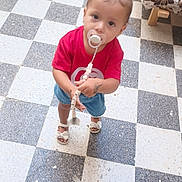 Lilia participe au concours pour gagner de l'argent avec cette photo : toddler, child, pacifier, pigtails, red_shirt, denim_shorts, sandals, floor, checkered_floor, indoor, curious, standing, looking_up, beaded_clip, furniture, sofa, pattern, young_child, cute, portrait