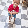 toddler, child, pacifier, pigtails, red_shirt, denim_shorts, sandals, floor, checkered_floor, indoor, curious, standing, looking_up, beaded_clip, furniture, sofa, pattern, young_child, cute, portrait