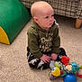 baby, child, sitting, indoor, carpet, toy, hoodie, plaid_couch, floor, curious, colorful, patterned_pants, furniture, playtime, young_child, soft_lighting, home, cozy, infant, casual_clothing