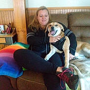 Kloeanne is registered to the contest to win money with this photo: black_clothing, blanket, brown_couch, casual_clothing, comfortable, couch, dog, footwear, happy_dog, home, indoor, leisure, pet, rainbow_blanket, relaxed, seated, shoe, smiling, woman, wood_paneling