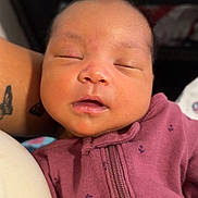Zharya joined the competition — help win amazing prizes! baby, sleeping, infant, maroon_clothing, onesie, face, closeup, person, tattoo, arm, peaceful, indoors, soft_lighting, newborn, portrait, cute, child, skin, resting, cozy