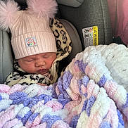 Finleigh is registered to the contest to win money with this photo: baby, newborn, car_seat, hat, pom_poms, blanket, sleeping, clothing, infant, child, leopard_print, pink, purple, white, soft_texture, cute, bundle, cozy, indoors, person