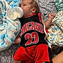 Grayson is registered to the contest to win money with this photo: baby, infant, bottle, feeding, clothing, jersey, red_shorts, blanket, bedspread, patterned, lying_down, fist, foot, cute, cozy, indoors, milk, child, person, sleepwear