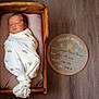 newborn, baby, swaddled, blanket, wooden_cradle, pillow, floor, sign, birth_details, indoor, infant, resting, cute, cozy, sleeping, person, portrait, child, soft_light, wood