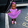child, girl, smiling, dress, pink_bow, beads, sandals, flower_sandals, parking_lot, car_door, license_plate, asphalt, white_line, standing, happy, outdoor, person, cute, fashion, accessories