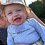 baby, child, smiling, blue_eyes, hat, bucket_hat, shirt, text_on_clothing, outdoor, sunlight, person, happy, holding, nature, greenery, arm, bracelet, portrait, cute, infant