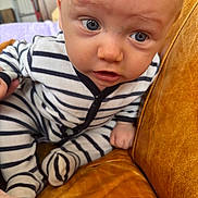 Jaïden a rejoint le concours — aidez-le/la à gagner de superbes lots ! baby, blue_eyes, child, closeup, couch, curious, expression, face, furniture, home, indoor, infant, leather, onesie, person, seated, skin, small_hand, striped_clothing, young_child
