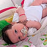 baby, infant, pacifier, white_onesie, blanket, floral_pattern, red_bracelet, cute, lying_down, close_up, indoors, soft_lighting, sleepwear, newborn, child, face, skin, hand, comfort, resting