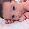 baby, close_up, face, blue_eyes, curly_hair, red_bracelet, skin, hand, lying_down, blanket, infant, portrait, cute, child, newborn, soft_light, indoors, peaceful, resting, young