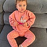 toddler, child, sitting, couch, gray_couch, pink_sweatshirt, fairy_design, floral_leggings, curly_hair, holding_object, indoor, cozy, cute, young_child, socks, casual_clothing, portrait, home, furniture, person