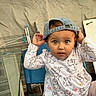 toddler, child, cap, denim_cap, blue_chair, cartoon_clothing, long_sleeve_shirt, curious_expression, indoor, face, person, seated, patterned_clothing, cute, baby, hands_up, light_brown_hair, large_eyes, playful, casual