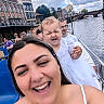 woman, baby, man, boat, river, bridge, historic_building, water, sky, clouds, people, smile, outdoor, daytime, selfie, white_clothing, happy, tourist, urban, travel