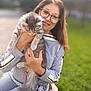 blurred_background, bokeh, cat, glasses, grass, grey_tabby, hands, happy, holding, leash, long_hair, outdoor, pet, portrait, purse, sitting, smiling, sunlight, sweater, woman