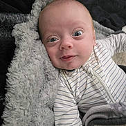 Mason is registered to the contest to win money with this photo: baby, infant, face, eyes, blanket, striped_clothing, onesie, cozy, soft_texture, cute, child, portrait, lying_down, closeup, expression, skin, head, small_person, warm, indoor