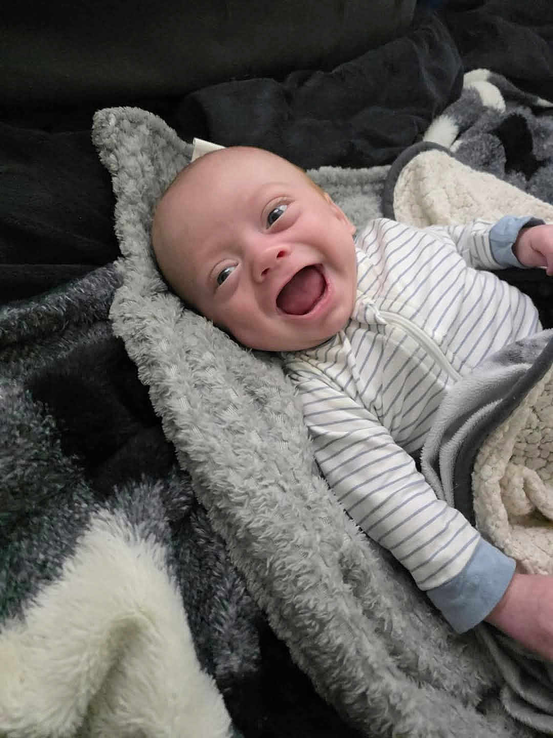 Mason is registered to the contest to win money with this photo: baby, infant, smiling, happy, blanket, cozy, clothing, striped, lying_down, face, child, cute, soft_texture, warm, indoor, newborn, joy, expression, skin, sleepwear