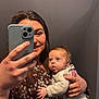 baby, child, woman, person, mirror, selfie, smartphone, hand, face, smile, tongue, clothing, long_hair, indoor, holding, cute, expression, background, casual, portrait