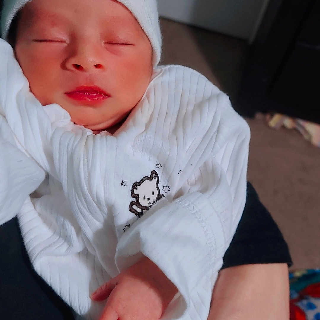 Jotherphen is registered to the contest to win money with this photo: baby, beanie, child, cozy, cradled, cute, hand, human, indoor, infant, newborn, peaceful, portrait, resting, sleeping, small_hand, soft_light, toddler, white_clothing, wrapped