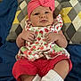 baby, infant, headband, pink, bow, strawberry_pattern, clothing, pillow, blanket, red_pants, white_socks, cute, portrait, indoor, child, person, lying_down, soft_fabric, colorful, comfortable