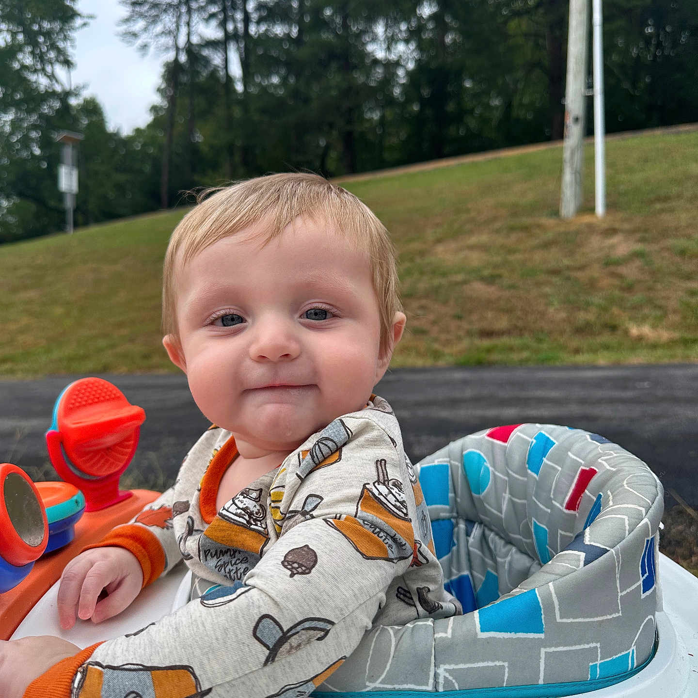 Darren joined the competition — help win amazing prizes! baby, child, infant, portrait, smiling, outdoor, activity_seat, toy, playground, grass, trees, park, road, lamppost, clothing, onesie, orange, blue, sitting, face