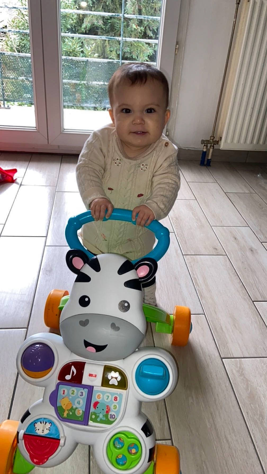 Alba participe au concours pour gagner de l'argent avec cette photo : baby, baby_products, baby_toddler_clothing, baby_toys, child, door, flooring, fun, happy, hardwood, head, leisure, person, room, sitting, smile, t_shirt, toddler, toy, window