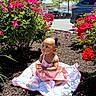 toddler, child, pink_dress, blanket, flowers, red_flowers, mulch, outdoor, daylight, trees, car, parking_lot, greenery, cute, baby, sitting, portrait, nature, sunlight, shoes