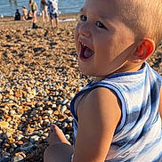 Tom is registered to the contest to win money with this photo: toddler, child, smiling, beach, pebbles, summer, sea, water, sunlight, casual_clothing, outdoor, happy, person, nature, vacation, relaxation, fun, family, daytime, shore