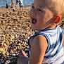 toddler, child, smiling, beach, pebbles, summer, sea, water, sunlight, casual_clothing, outdoor, happy, person, nature, vacation, relaxation, fun, family, daytime, shore