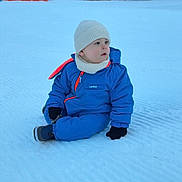 Adélio a rejoint le concours — aidez-le/la à gagner de superbes lots ! toddler, child, snow, winter_clothing, blue_snowsuit, knit_hat, gloves, outdoor, forest, pine_trees, snow_field, winter, cold_weather, sitting, curious, scenic, nature, daylight, red_netting, boots