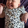 baby, infant, onesie, floral_pattern, smiling, tongue_out, lying_down, purple_blanket, cute, chubby, skin, head, hand, arm, face, person, child, expression, indoors, adorable