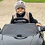 élyo participe au concours pour gagner de l'argent avec cette photo : toddler, child, toy_car, pacifier, hat, pom_pom, vest, black_clothing, outdoor, driveway, steering_wheel, cute, portrait, baby, vehicle, small_car, face, smile, person, fun