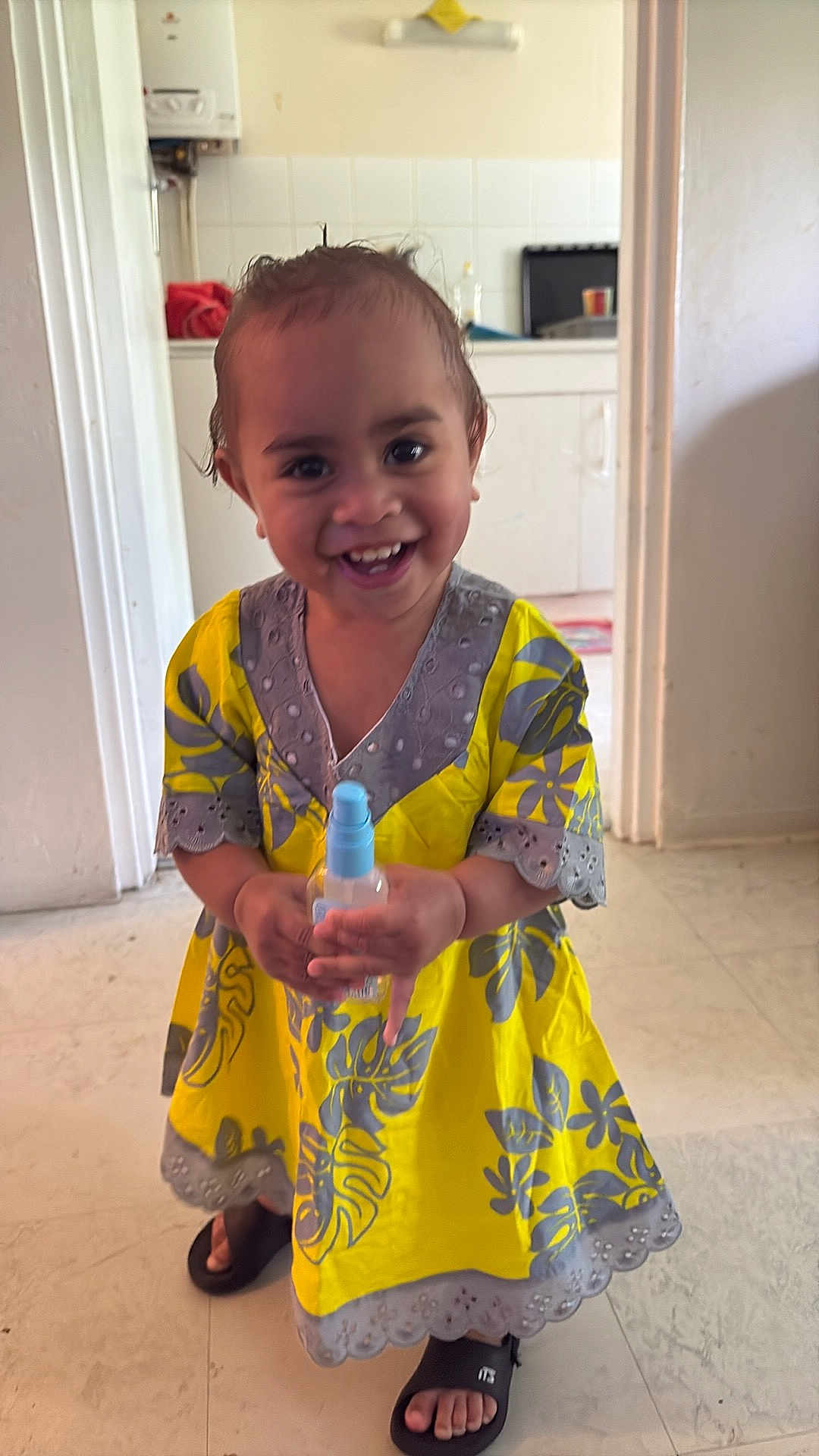 Cinéné a rejoint le concours — aidez-le/la à gagner de superbes lots ! toddler, child, smiling, yellow_dress, indoor, floor, spray_bottle, wet_hair, slippers, kitchen, cabinet, doorway, person, happy, standing, playful, cute, young_child, home, portrait