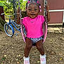 Armani is registered to the contest to win money with this photo: toddler, child, swing, outdoor, playground, pink_shirt, braided_hair, hair_accessories, sneakers, bicycle, tree, shed, grass, dirt, sunlight, happy, smiling, person, play, summer