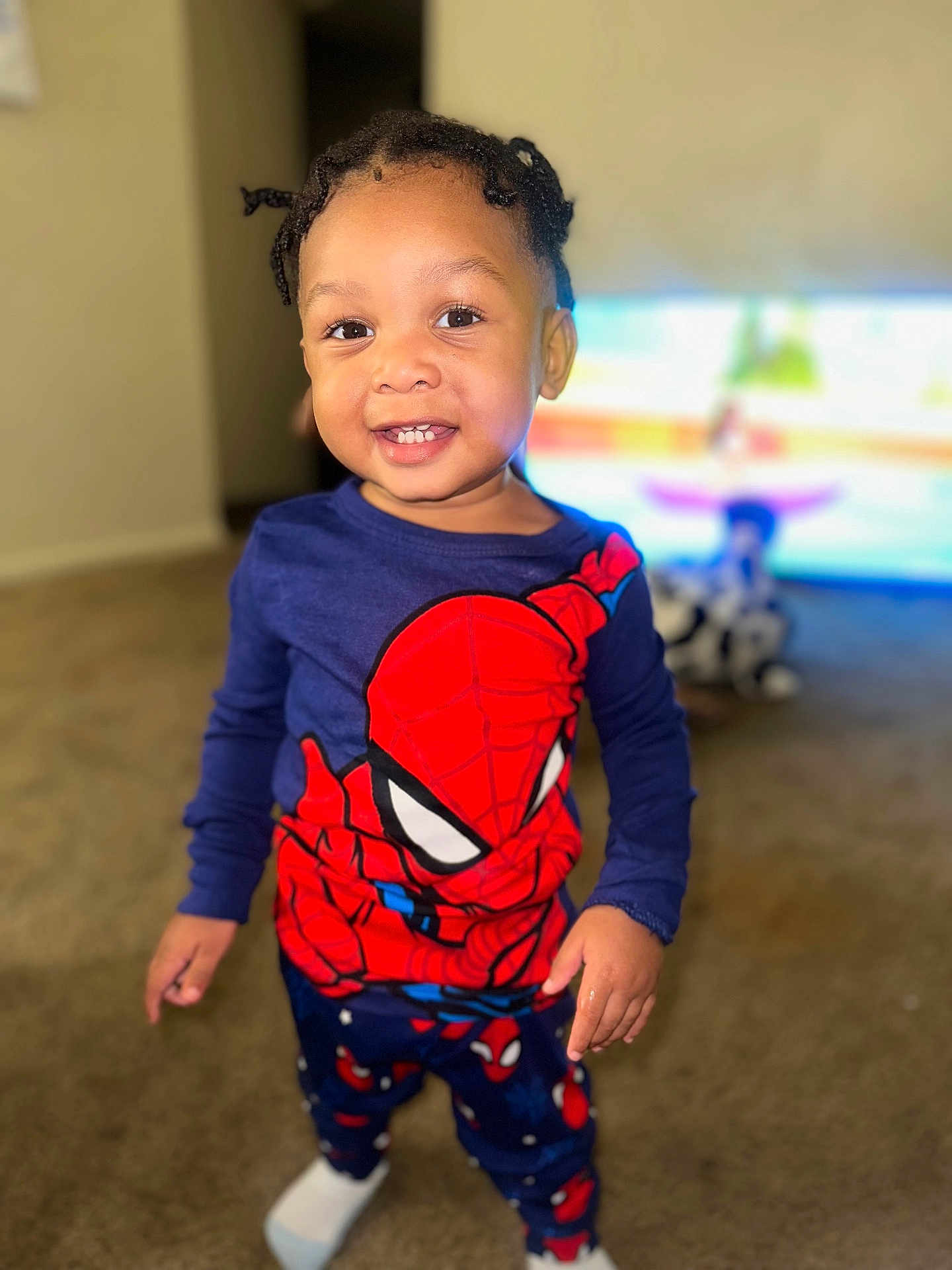Quintrell is registered to the contest to win money with this photo: child, toddler, smile, face, indoor, carpet, pajamas, spiderman, clothing, person, happy, cute, standing, hair, eyes, socks, room, television, blurred_background, home