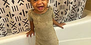 Quintrell is registered to the contest to win money with this photo: toddler, child, smiling, barefoot, bathroom, bathtub, shower_curtain, pattern, floor_tile, black_mat, clothing, striped_dress, hair, braids, happy, standing, young_child, indoors, person, cute