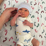 Wyatt is registered to the contest to win money with this photo: newborn, baby, infant, hand, blanket, footprints, onesie, hat, human, skin, cute, lying_down, pattern, blue, white, pink, red, green, yellow, toddler