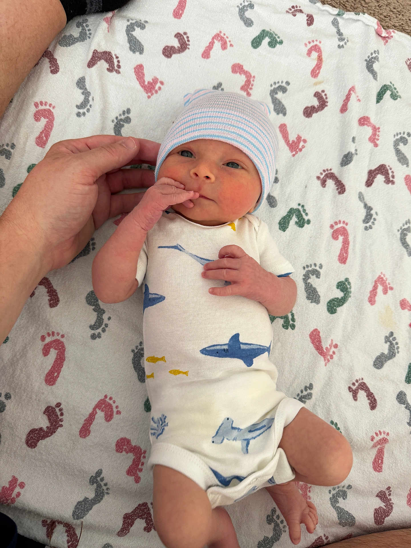 Wyatt is registered to the contest to win money with this photo: newborn, baby, infant, hand, blanket, footprints, onesie, hat, human, skin, cute, lying_down, pattern, blue, white, pink, red, green, yellow, toddler