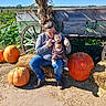 Hunter is registered to the contest to win money with this photo: baby, child, parent, family, pumpkin_patch, pumpkins, hay_bales, wagon, corn_stalk, farm, outdoor, autumn, harvest, rural, sitting, portrait, smiling, baby_clothing, daylight, rustic