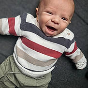 Sorën participe au concours pour gagner de l'argent avec cette photo : baby, smiling, striped_sweater, pants, white_shoes, happy, child, infant, portrait, cute, lying_down, clothing, toddler, face, person, indoor, cozy, apparel, casual_wear, expression