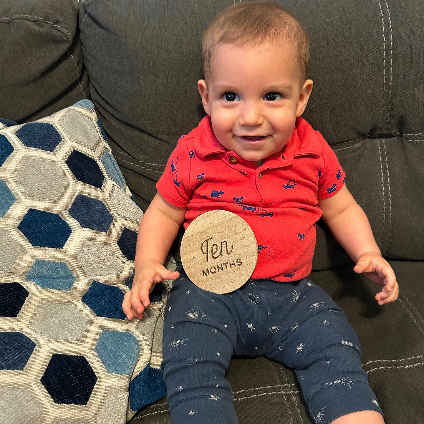 Miles joined the competition — help win amazing prizes! baby, blue_pants, child, couch, cute, fabric, furniture, happy, home, indoor, infant, patterned_pants, person, pillow, portrait, red_shirt, seated, smiling, ten_months, wooden_sign