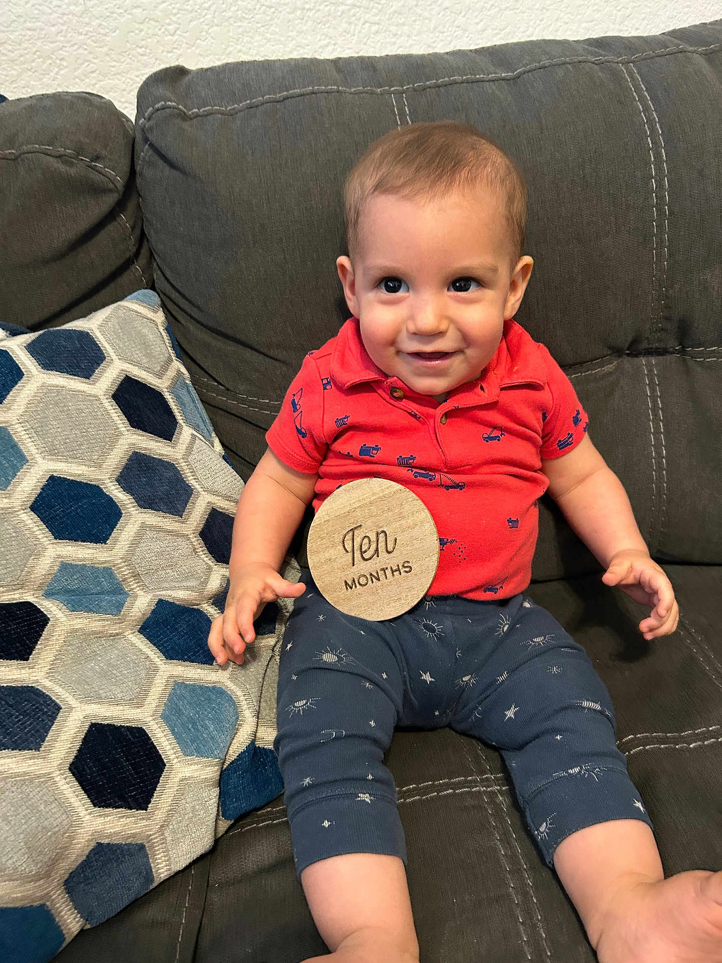 Miles joined the competition — help win amazing prizes! baby, child, smiling, couch, pillow, red_shirt, blue_pants, patterned_pants, wooden_sign, ten_months, indoor, happy, person, seated, cute, portrait, home, furniture, fabric, infant