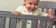 Miles joined the competition — help win amazing prizes! baby, crib, onesie, baby_clothes, hand, railing, pink_blanket, indoor, child, smiling, face, person, bedroom, furniture, happy, standing, infant, home, cute, playful