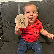 Miles is registered to the contest to win money with this photo: baby, child, infant, smiling, couch, red_shirt, blue_pants, celestial_prints, wooden_sign, ten_months, happy, sitting, indoors, person, face, hand, furniture, home, cute, portrait